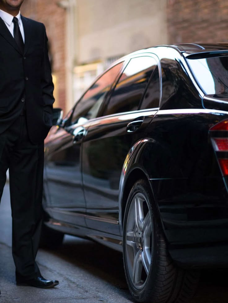 Uniformed executive driver standing by premium black car service